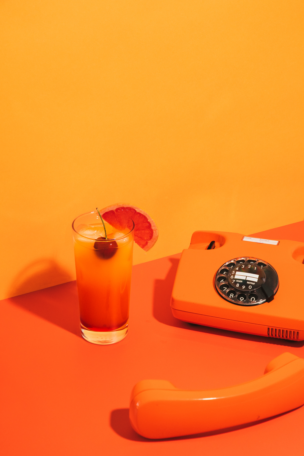 Glass of Cocktail and Telephone on Orange Background